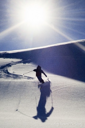 A telemark skier turns down a slope with the sun behind.