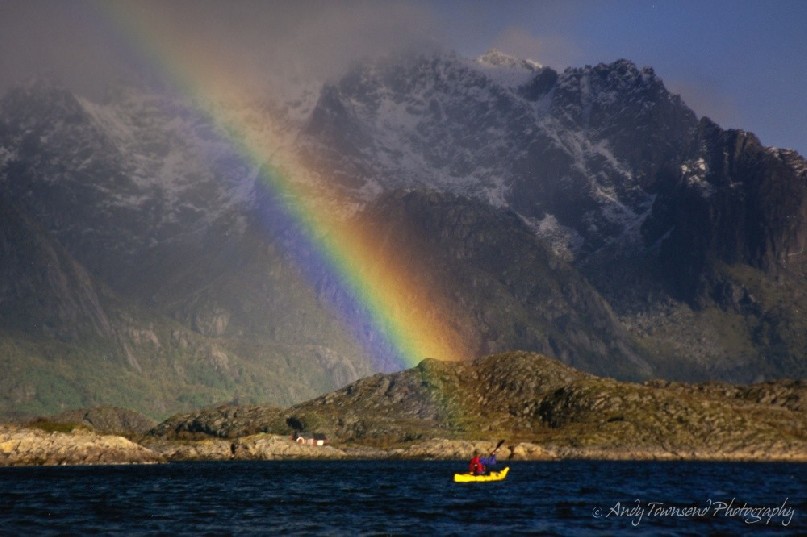 Light rain over a kayaker catches the sun creating a beautiful rainbow in a Nowegian fjord.
