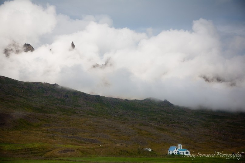 A lone farmhouse is dwarfed by the surrounding misty mountains.
