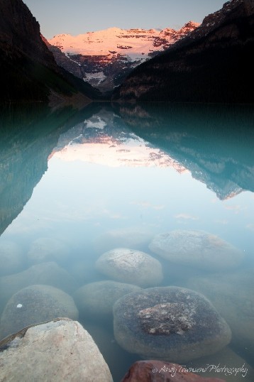 A sunrise glow hits a distant range and reflects into Lake Louise.