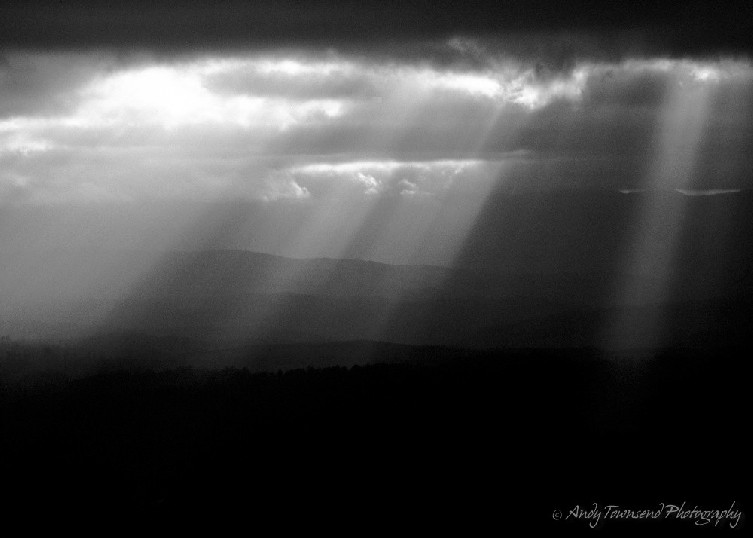 Crepuscular rays stream through gaps in clouds over  distant ridgelines.