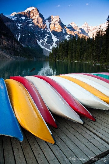 A line of colourful canoes on a jetty with Moraine Lake and the Ten Peaks in the distance.