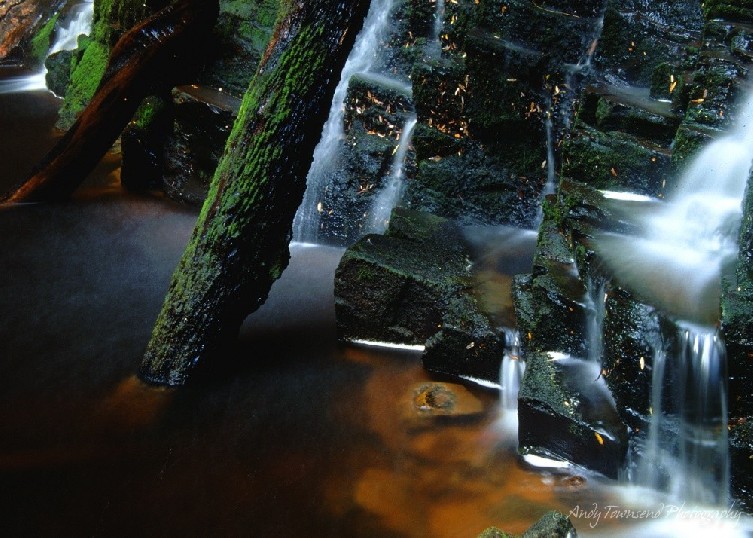 A long exposure of water falling over mossy rocks.