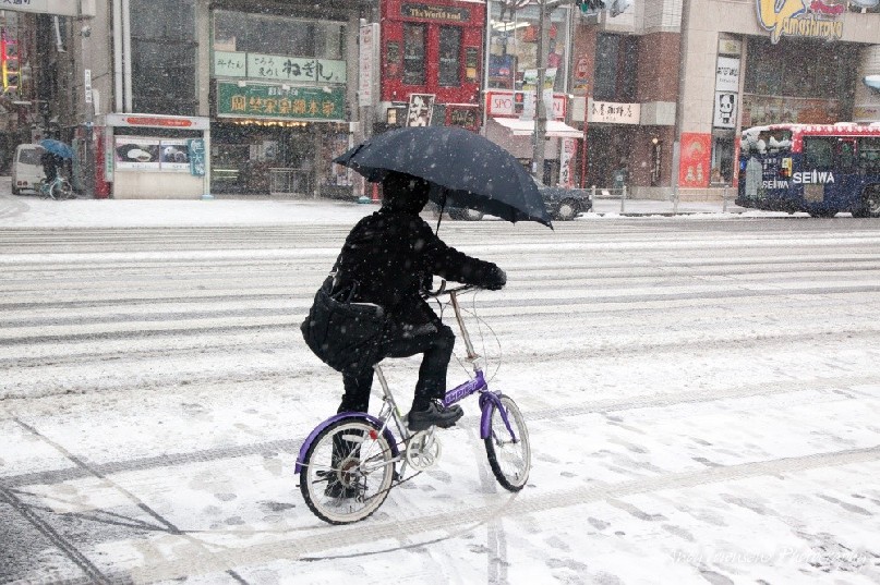 A cyclist in Ueno rides with an umbrella through the snowy streets.
