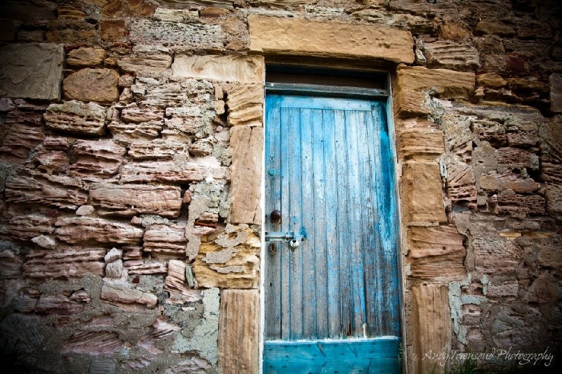A weathered blue door sits in sharp contrast to this rough, eroded sandstone wall of this cottage.