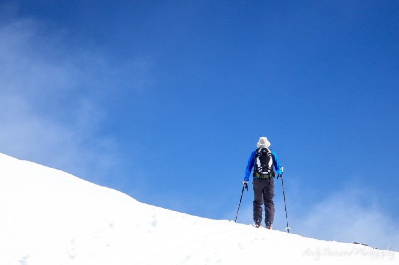 A skier makes their way across a ridgeline with a clearing blue sky above.
