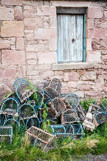 A pile of crab pots sits outside the weathered sandstone wall of this cottage.