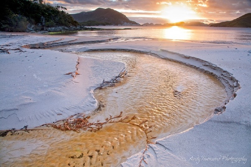 As the sun sets over the Breaksea Islands, a small tannin stream trickles into the tranquil Bramble Cove in Tasmania's Southwest National Park.