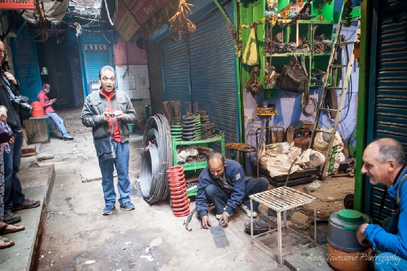 A tour guide talking next to a small metal workshop in a alley.