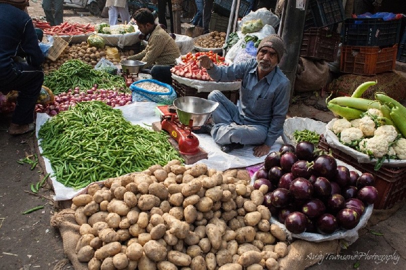 A man siting at his stall selling vegetables in a whole street market.