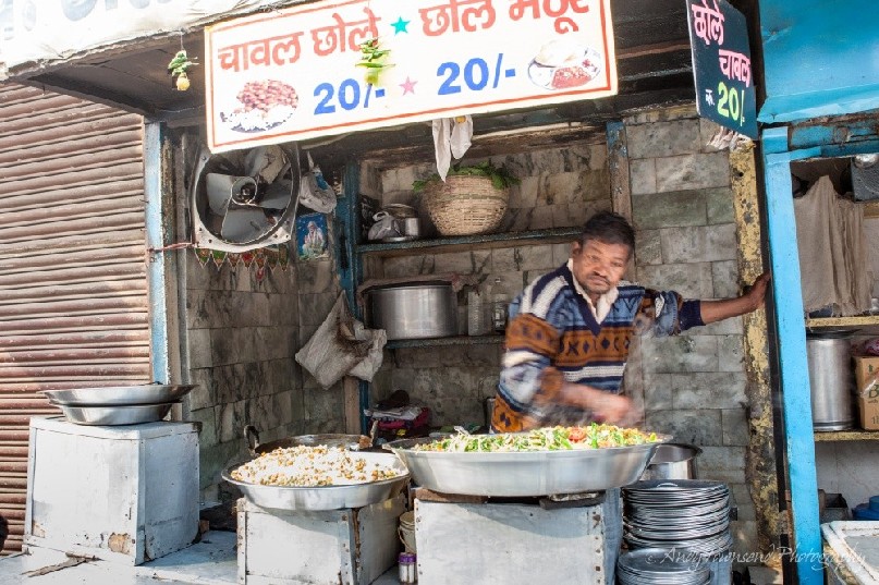 A man looks over a large pot of cooking vegetables in a rodside stall.