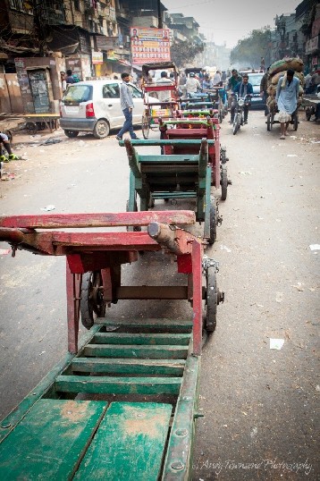 A large line of colourful wooden trolleys divides a busy street in Delhi.