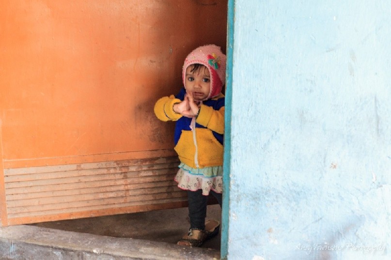 A baby girl in her mother's shoes looks out of a door above the spice market.