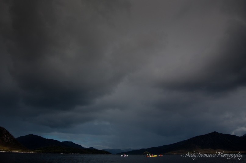 Storm clouds roll in over a group of sea kayakers in Bathurst Harbour, Southwest National Park, Tasmania.