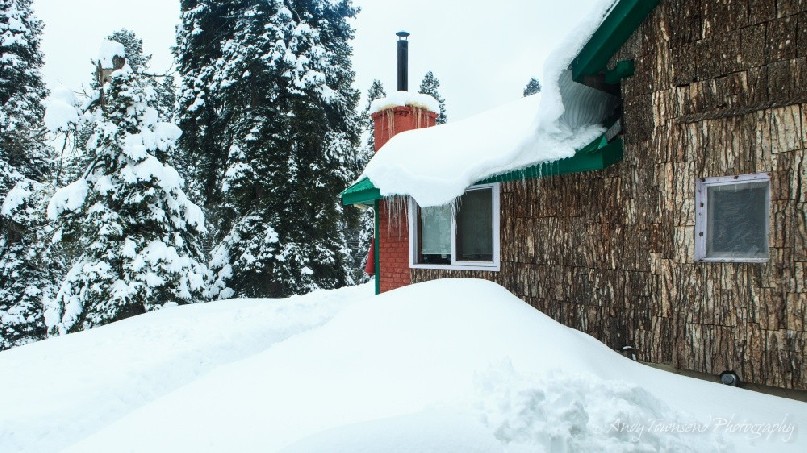 The exterior bark wall and chimney of one of the bedrooms in the hotel surrounded by deep snow.