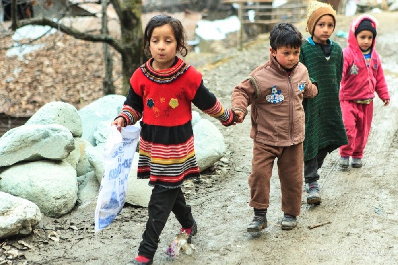 A group of four children walk hand-in-hand along a dirt track between Drung and Targmarg villages.