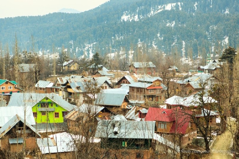 View over Tangmarg village with winter snow on the forested hillside behind.