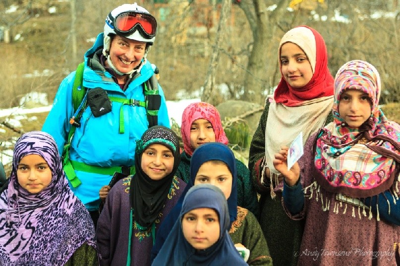 A female skier and a group of traditionally dressed young village girls pause for a portrait.