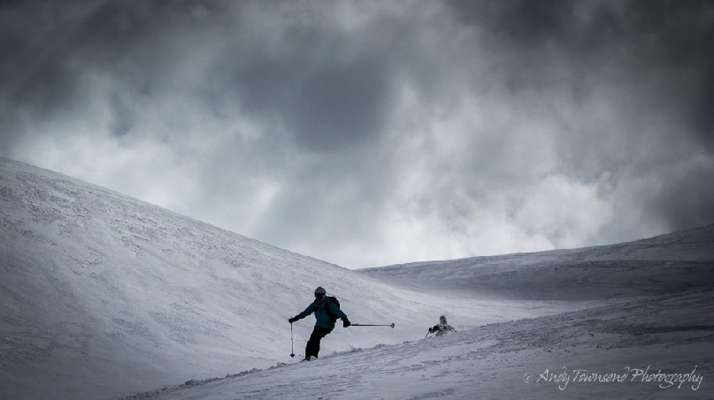 A female alpine skier making their way down an open slope with dark clouds above.