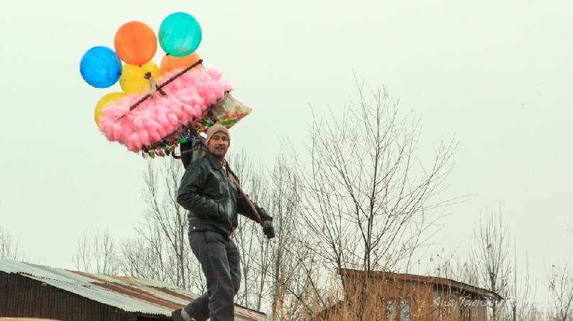 A man carrying a load of fairy-floss candy and balloons over his shoulder.