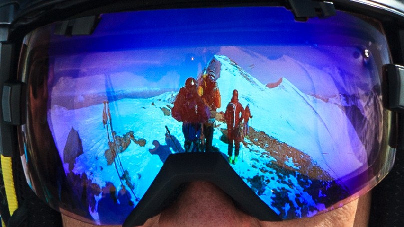 A close up of goggles reflecting people and a distant mountain range.