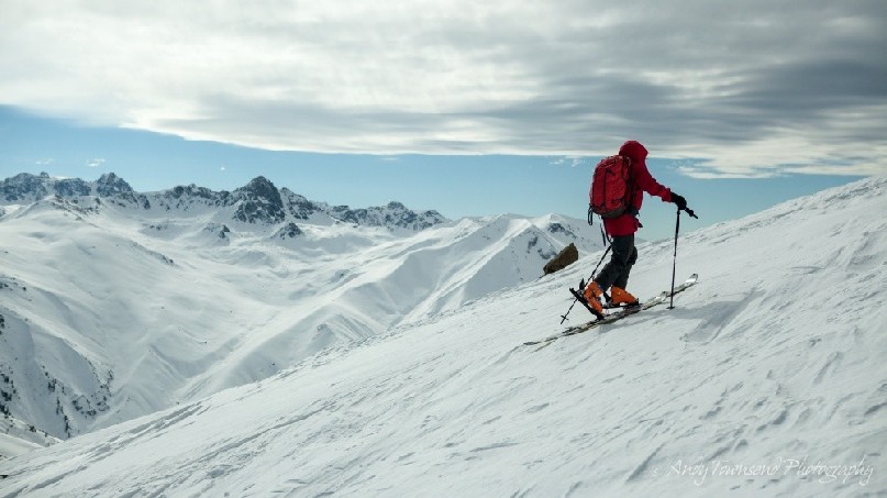 A skier skinning up towards the summit of Mt Apharwat with distant mountain range behind.