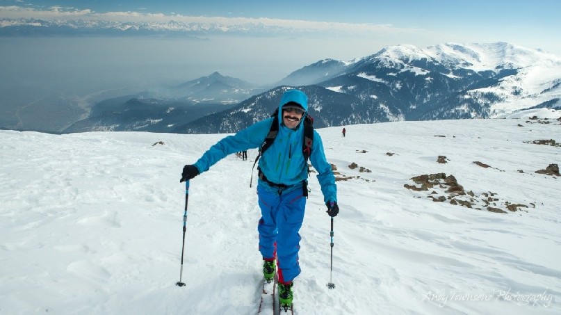 A smiling skier makes their way towards the summit of Mt Apharwat with distant fog in the valley below.