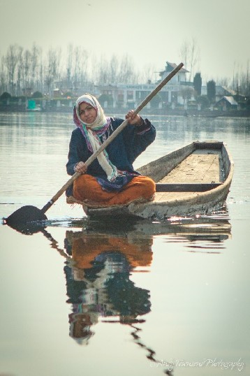 A young woman balances elegantly on the edge of a  wooden boat in Dal Lake.
