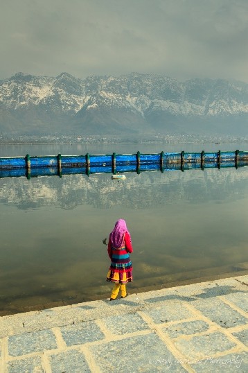 A young girl in colorful dress pauses on the steps with snow-covered mountains in the distance.